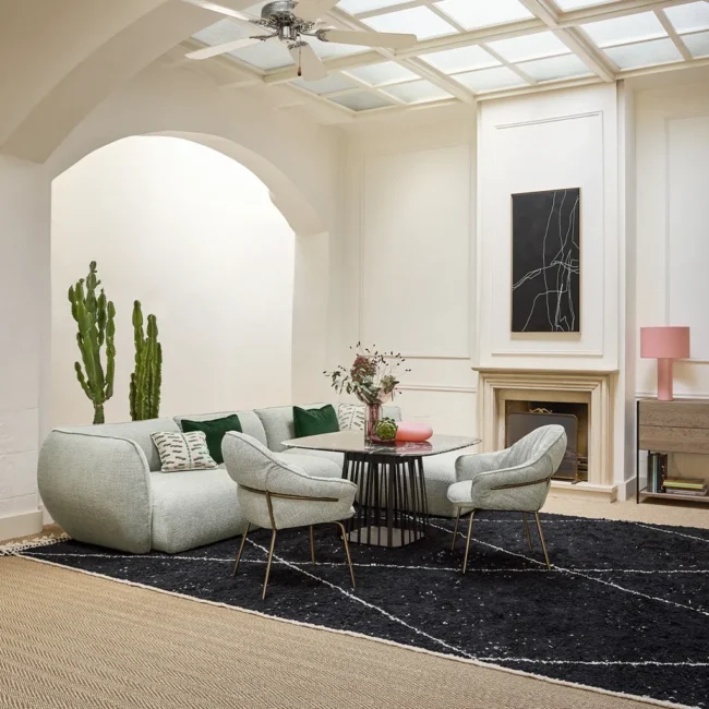 Moderne Wohnzimmereinrichtung mit einem runden Tisch, zwei Sesseln und einem Sofa, umgeben von Pflanzen und einem Kamin.