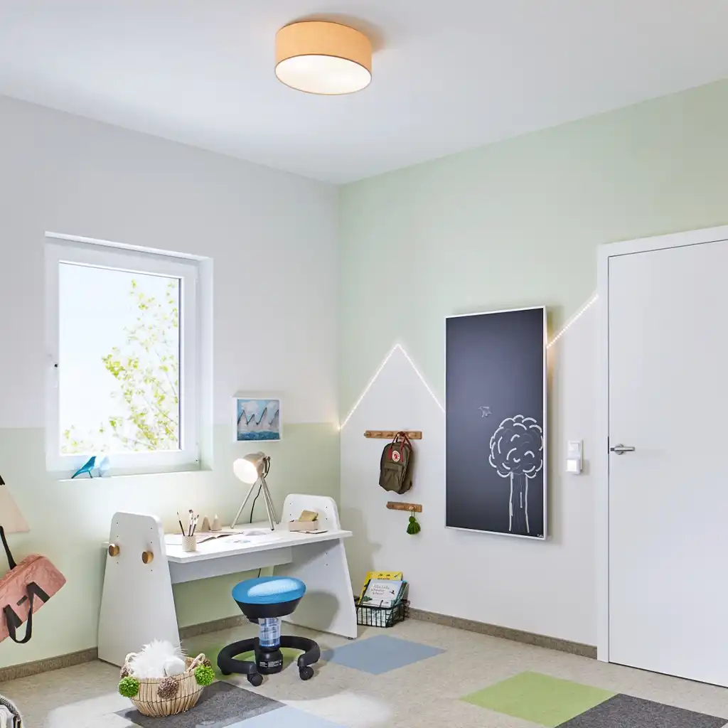Helles Kinderzimmer mit einem Schreibtisch, einer Lampe und einem Fenster. An der Wand hängt eine Tafel.