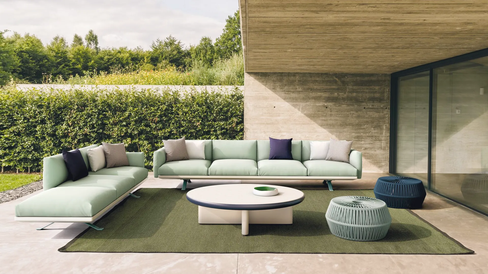 Moderne Gartenmöbel mit mintgrüner Couch, runden Tischen und einem Teppich auf einer Terrasse.