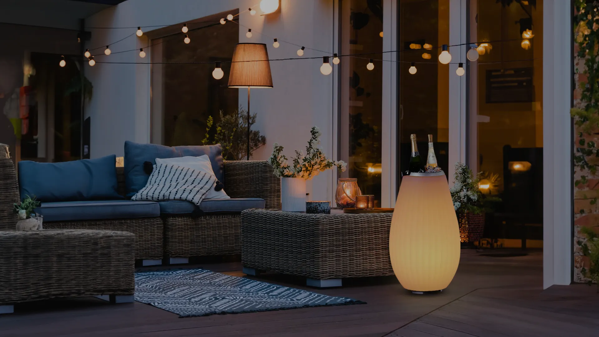 Gemütlicher Außenbereich mit einem runden, leuchtenden LED-Flaschenkühler, einer Couch und Lichterketten.